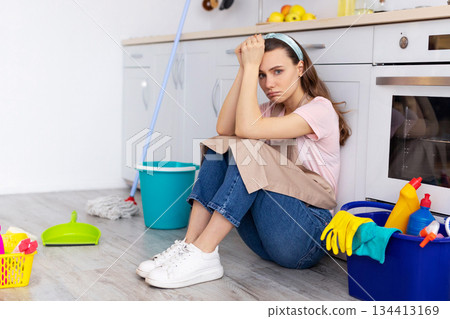 Housewife depression. Sad young lady feeling trapped with household duties, ready to cry, sitting on kitchen floor with cleaning supplies. Millennial woman tired of domestic work Housewife depression. Sad young lady feeling trapped with household duties, ready to cry, sitting on kitchen floor with cleaning supplies. Millennial woman tired of domestic work 134413169
