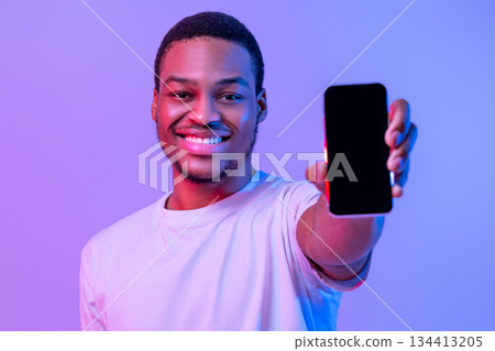 Handsome African American Guy Showing Smartphone With Black Blank Screen At Camera, Demonstrating Free Copy Space For App Or Website Design, Standing In Neon Light Over Purple Background, Mockup Handsome African American Guy Showing Smartphone With Black Blank Screen At Camera, Demonstrating Free Copy Space For App Or Website Design, Standing In Neon Light Over Purple Background, Mockup 134413205