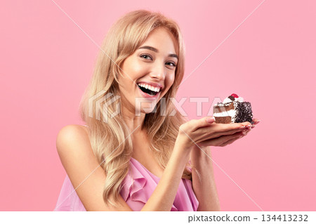 Pretty Caucasian woman holding yummy cake, smiling and looking at camera on pink studio background. Beautiful blonde woman celebrating birthday, enjoying delicious dessert Pretty Caucasian woman holding yummy cake, smiling and looking at camera on pink studio background. Beautiful blonde woman celebrating birthday, enjoying delicious dessert 134413232