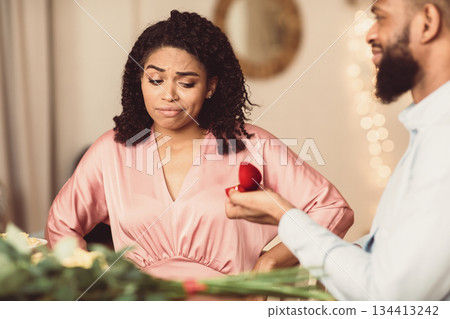 Unsuccessful Proposal Concept. Hopeful african american man proposing to confused doubtful woman who is hesitating, lady looking frustrated thinking about refusal, not sure about marriage 134413242