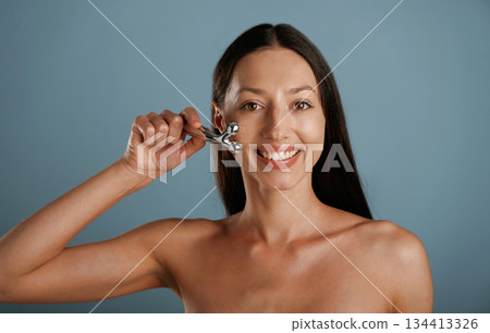 Skin massager. Young woman is in the studio against background Skin massager. Young woman is in the studio against background 134413326