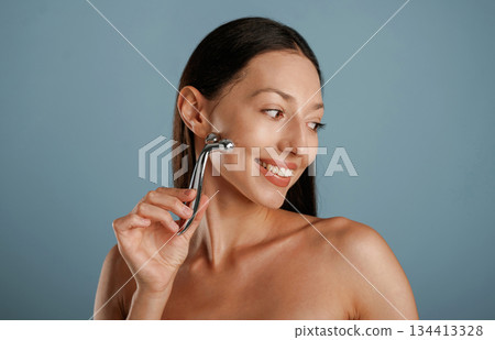 Skin massager. Young woman is in the studio against background Skin massager. Young woman is in the studio against background 134413328