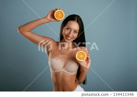Oranges in hands. Young woman is in the studio against background 134413346