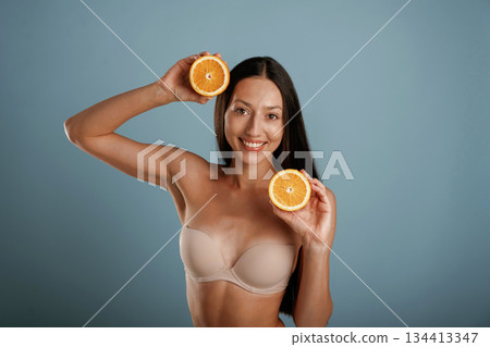 Oranges in hands. Young woman is in the studio against background Oranges in hands. Young woman is in the studio against background 134413347