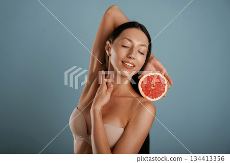 Grapefruit, conception of healthy eating. Young woman is in the studio against background Grapefruit, conception of healthy eating. Young woman is in the studio against background 134413356
