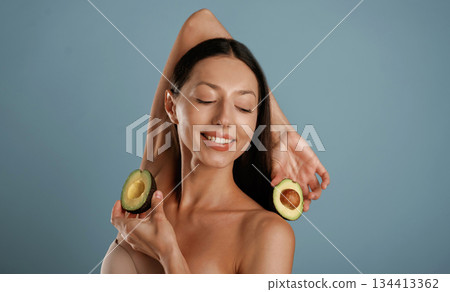Avocado in hands. Young woman is in the studio against background Avocado in hands. Young woman is in the studio against background 134413362