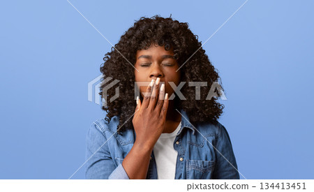 Tired african american young curly woman yawning on yellow studio background, sleepy inattentive deprived black female feeling somnolent lazy bored gaping suffering from lack of sleep, closeup 134413451