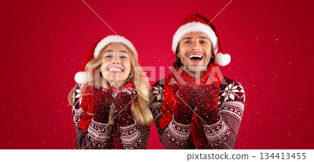 Christmas time. Happy millennial guy and his girlfriend blowing snow on red background 134413455