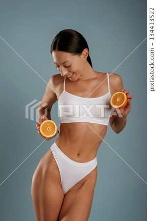 Skinny body, diet conception, with oranges. Young woman is in the studio against background 134413522