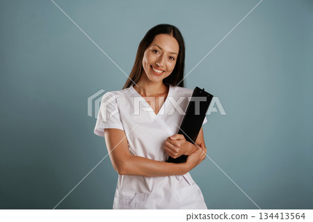 In professional lab coat, nurse is standing. Young woman is in the studio against background 134413564