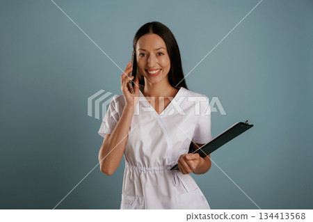 In professional lab coat, nurse is standing. Young woman is in the studio against background 134413568