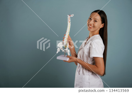 Nurse is holding spine model in hands. Young woman is in the studio against background 134413569