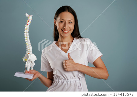 Nurse is holding spine model in hands. Young woman is in the studio against background Nurse is holding spine model in hands. Young woman is in the studio against background 134413572