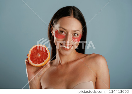 Red patches under eyes, holding grapefruit. Young woman is in the studio against background Red patches under eyes, holding grapefruit. Young woman is in the studio against background 134413603