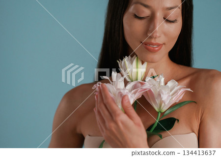 Posing with lily flower. Young woman is in the studio against background 134413637