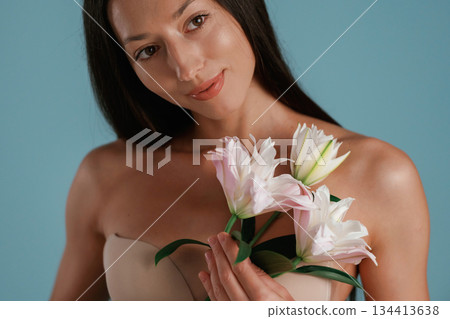 Posing with lily flower. Young woman is in the studio against background Posing with lily flower. Young woman is in the studio against background 134413638