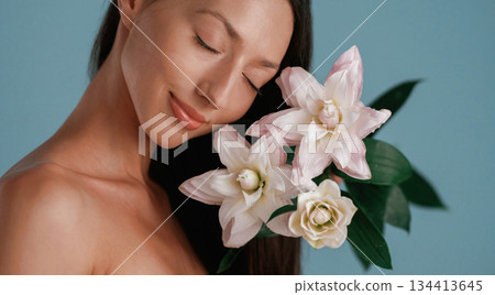 Soft feel, holding lily flower. Young woman is in the studio against background Soft feel, holding lily flower. Young woman is in the studio against background 134413645