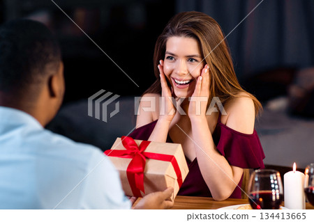 Gift For You. Loving Black Man Making Romantic Surprise To Girlfriend During Dinner In Restaurant, Giving Wrapped Present Box With Red Ribbon, Surprised Woman Touching Face In Excitement, Close Up Gift For You. Loving Black Man Making Romantic Surprise To Girlfriend During Dinner In Restaurant, Giving Wrapped Present Box With Red Ribbon, Surprised Woman Touching Face In Excitement, Close Up 134413665