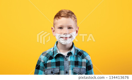 Playful little young boy shaving face over yellow studio background, imitating his dad, copy space. Cute redhead kid with shaving foam on his face smiling at camera, acting like adult man Playful little young boy shaving face over yellow studio background, imitating his dad, copy space. Cute redhead kid with shaving foam on his face smiling at camera, acting like adult man 134413676