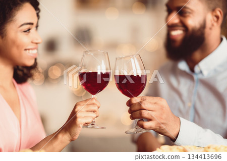 Cheers. Closeup of beautiful smiling young american couple drinking red wine, holding glasses and toasting, having romantic dinner, spending time together. Young black family celebrating 134413696