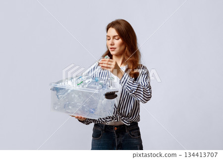 Young Beautiful Woman Putting Plastic Bottles To Container In Her Hands, Millennial Lady Collecting Waste For Recycling, Eco-Activist Sorting Garbage Over Light Studio Background, Copy Space Young Beautiful Woman Putting Plastic Bottles To Container In Her Hands, Millennial Lady Collecting Waste For Recycling, Eco-Activist Sorting Garbage Over Light Studio Background, Copy Space 134413707