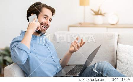 Cheerful Guy Talking On Phone Sitting With Laptop Computer On Sofa At Home. Modern Communication And Lifestyle. Happy Man Chatting On Cellphone And Laughing Indoors Cheerful Guy Talking On Phone Sitting With Laptop Computer On Sofa At Home. Modern Communication And Lifestyle. Happy Man Chatting On Cellphone And Laughing Indoors 134413709