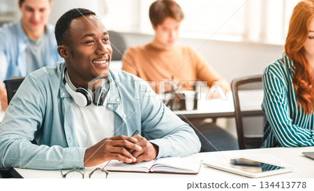 Return To Education Concept, First Day Of Highschool. Portrait Of Smiling African American Male Student Listening To Lecturer at University, Sitting At Desk In Classroom With Multiethnic Classmates 134413778