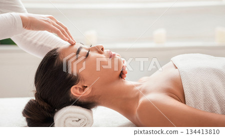 Masseur doing acupressure massage to young asian woman, pressing on her forehead. Relaxed korean lady enjoying wellness day at spa salon, having beauty treatments at cosmetology cabinet, side view 134413810