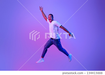 Excited Funny Black Guy Jumping Up In Neon Light Over Purple Background, Full-Length Portrait In Motion Of Euphoric African American Man Jump In The Air With Open Mouth And Raised Hands, Copy Space Excited Funny Black Guy Jumping Up In Neon Light Over Purple Background, Full-Length Portrait In Motion Of Euphoric African American Man Jump In The Air With Open Mouth And Raised Hands, Copy Space 134413888