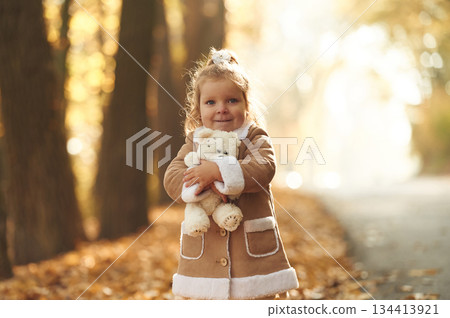 In the autumn forest. Cute little girl is with teddy bear in hands In the autumn forest. Cute little girl is with teddy bear in hands 134413921
