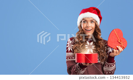 Christmas surprise. Gorgeous millennial woman in Santa hat opening heart shaped gift box on blue studio background, panorama. Young lady excited to receive her Xmas present Christmas surprise. Gorgeous millennial woman in Santa hat opening heart shaped gift box on blue studio background, panorama. Young lady excited to receive her Xmas present 134413932