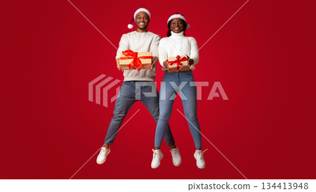 Joyful Black Couple In Santa Hats Jumping With Christmas Gift Boxes In Hands, Holding Xmas Presents And Having Fun Together Over Orange Background, Enjoying Celebrating Winter Holidays, Full Length Joyful Black Couple In Santa Hats Jumping With Christmas Gift Boxes In Hands, Holding Xmas Presents And Having Fun Together Over Orange Background, Enjoying Celebrating Winter Holidays, Full Length 134413948