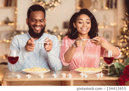 Excited young african american couple sitting in restaurant and taking pictures of food with mobile phones for social media, foodie bloggers celebrating St Valentine's Day together Excited young african american couple sitting in restaurant and taking pictures of food with mobile phones for social media, foodie bloggers celebrating St Valentine's Day together 134413953