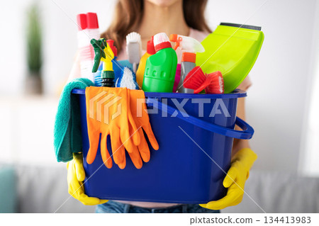 Unrecognizable millennial maid holding bucket with cleaning supplies indoors, closeup of hands. Cropped view of housewife with detergents, ready for house cleanup. Sanitary service concept 134413983