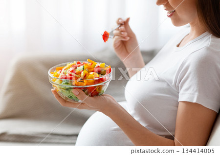 Unrecognizable Pregnant Lady Eating Fresh Vegetarian Salad From Bowl, Enjoying Healthy Nutrition And Organic Vitamin Food During Pregnancy, Sitting On Couch In Living Room, Side View, Cropped Shot Unrecognizable Pregnant Lady Eating Fresh Vegetarian Salad From Bowl, Enjoying Healthy Nutrition And Organic Vitamin Food During Pregnancy, Sitting On Couch In Living Room, Side View, Cropped Shot 134414005