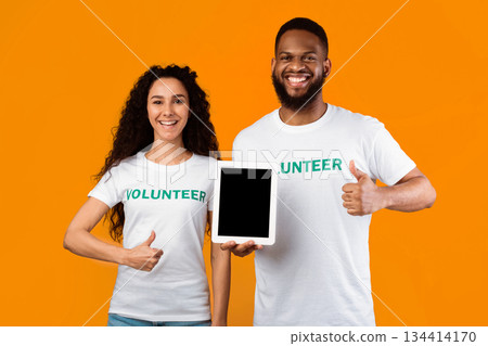 Couple Of Multiracial Volunteers Holding Tablet Computer With Empty Screen Gesturing Thumbs Up Standing On Yellow Background, Smiling To Camera. Studio Shot, Mockup Couple Of Multiracial Volunteers Holding Tablet Computer With Empty Screen Gesturing Thumbs Up Standing On Yellow Background, Smiling To Camera. Studio Shot, Mockup 134414170