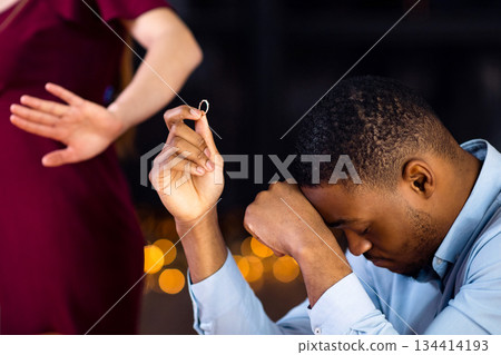 Unsuccessful Proposal Concept. Woman Rejecting Engagement Ring And Leaving Boyfriend, Desperate African American Guy Sitting At Table In Restaurant, Feeling Depressed And Lonely, Cropped Image Unsuccessful Proposal Concept. Woman Rejecting Engagement Ring And Leaving Boyfriend, Desperate African American Guy Sitting At Table In Restaurant, Feeling Depressed And Lonely, Cropped Image 134414193