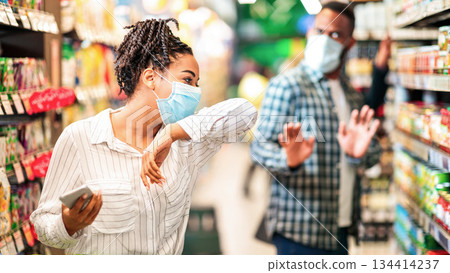 Sick Black Lady In Mask On Grocery Shopping Coughing In Elbow Buying Food Walking With Shop Cart Choosing Groceries In Supermarket Store Indoor. Social Distancing. Shop Safe During Covid-19 Pandemic Sick Black Lady In Mask On Grocery Shopping Coughing In Elbow Buying Food Walking With Shop Cart Choosing Groceries In Supermarket Store Indoor. Social Distancing. Shop Safe During Covid-19 Pandemic 134414237