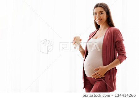 Healthy Drinks During Pregnancy. Portrait Of Smiling Young Pregnant Woman Holding Glass With Milk While Standing Near Window At Home, Happy Expectant Lady Enjoying Calcium Drink, Copy Space Healthy Drinks During Pregnancy. Portrait Of Smiling Young Pregnant Woman Holding Glass With Milk While Standing Near Window At Home, Happy Expectant Lady Enjoying Calcium Drink, Copy Space 134414260