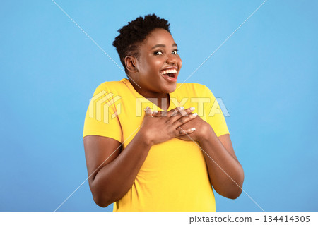 Excited Oversized African American Lady Posing Holding Hands On Chest Smiling Looking At Camera In Excitement Standing Over Blue Studio Background. Pleasant Surprise, Positive Emotions Concept 134414305