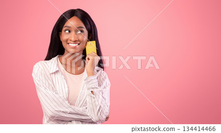Portrait of thoughtful African American lady with credit card recommending bank services on pink studio background. Happy young black woman promoting contactless shopping Portrait of thoughtful African American lady with credit card recommending bank services on pink studio background. Happy young black woman promoting contactless shopping 134414466