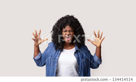 Furious young black woman raising hands up and screaming, showing her negative emotions over grey studio background. Emotional african american lady expressing anger or annoying 134414514