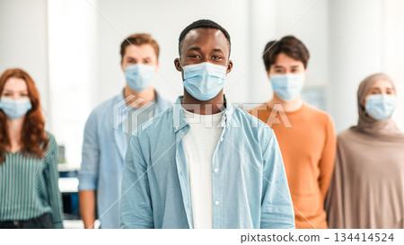 New Reality And Epidemic Concept. Diverse group of international people wearing protective medical masks, standing indoors, posing and looking at camera. Selective focus on african american man New Reality And Epidemic Concept. Diverse group of international people wearing protective medical masks, standing indoors, posing and looking at camera. Selective focus on african american man 134414524