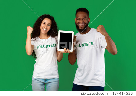 Two Multiethnic Volunteers Showing Digital Tablet Empty Screen Gesturing Yes Celebrating Success Standing Over Green Studio Background, Smiling To Camera. Activists Recommending Volunteering Website Two Multiethnic Volunteers Showing Digital Tablet Empty Screen Gesturing Yes Celebrating Success Standing Over Green Studio Background, Smiling To Camera. Activists Recommending Volunteering Website 134414536