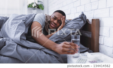 Unhappy Sick African American Guy Taking Medication Having Fever And Headache Lying In Bed At Home. Flu, Influenza And Covid-19 Medical Treatment Concept. Selective Focus Unhappy Sick African American Guy Taking Medication Having Fever And Headache Lying In Bed At Home. Flu, Influenza And Covid-19 Medical Treatment Concept. Selective Focus 134414562
