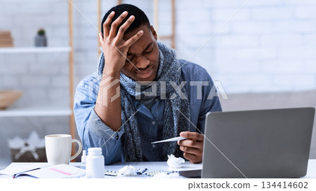Sick At Work. Ill African Man Having Fever Holding Thermometer Sitting At Workplace In Office. Influenza, Seasonal Cold And Coronavirus, Covid-19 Symptoms Concept Sick At Work. Ill African Man Having Fever Holding Thermometer Sitting At Workplace In Office. Influenza, Seasonal Cold And Coronavirus, Covid-19 Symptoms Concept 134414602