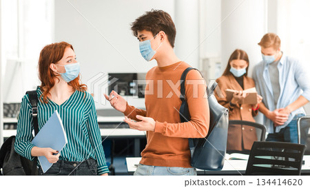 Portrait of asian man and red-haired woman standing in auditorium and talking during break, having conversation and discussing group project or task. Students wearing surgical face masks and backpacks Portrait of asian man and red-haired woman standing in auditorium and talking during break, having conversation and discussing group project or task. Students wearing surgical face masks and backpacks 134414620