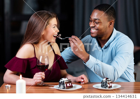 Loving African American Guy Sharing Dessert With His White Girfriend, Feeding Her With Fork, Romantic Multicultural Couple Enjoying Sweets And Drinking Wine While Dining Together, Free Space Loving African American Guy Sharing Dessert With His White Girfriend, Feeding Her With Fork, Romantic Multicultural Couple Enjoying Sweets And Drinking Wine While Dining Together, Free Space 134414631