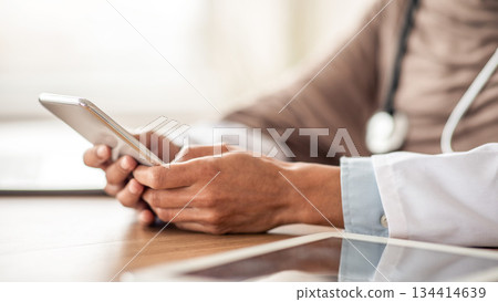 Cropped of female doctor using gadgets at workplace, holding smartphone and digital tablet. Unrecognizable therapist having online conversation with her patients, using mobile phone, closeup 134414639
