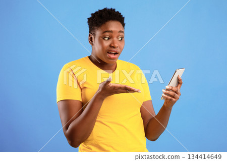 Discontented Black Lady Holding Smartphone Having Problem With Mobile Phone Or Waiting For Call Standing Over Blue Studio Background. Displeased Female Showing Cellphone Concept Discontented Black Lady Holding Smartphone Having Problem With Mobile Phone Or Waiting For Call Standing Over Blue Studio Background. Displeased Female Showing Cellphone Concept 134414649